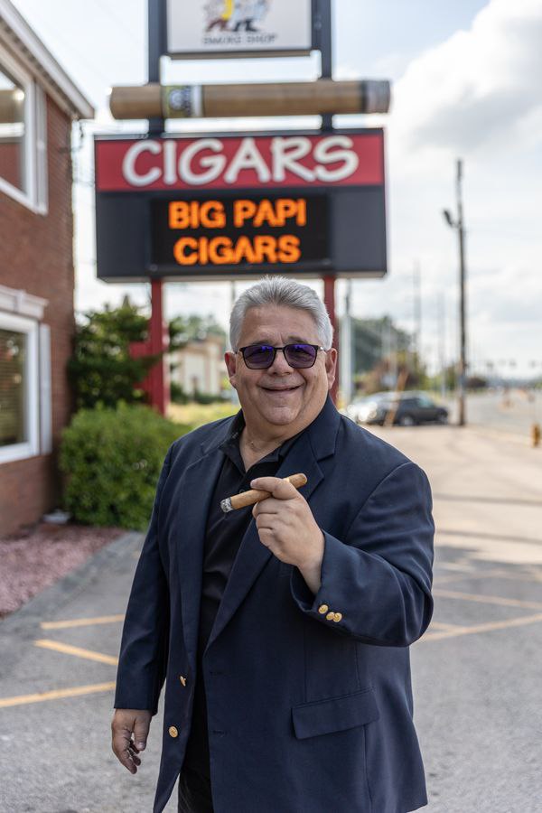 دیوید گاروفالو کیست؟ داستان زندگی رئیس سیگار و امپراتوری Two Guys Cigars 1 <h1>دیوید گاروفالو کیست؟ داستان زندگی رئیس سیگار و امپراتوری Two Guys Cigars</h1> در دنیای سیگار برگ، بعضی افراد به دلیل ساختن یک برند مشهور شناخته می شوند، بعضی به خاطر سال ها فعالیت در کارخانه ها و برخی دیگر به واسطه مجموعه های ارزشمند، رسانه ها یا نقششان در گسترش فرهنگ سیگار برگ. اما تعداد کمی از افراد توانسته اند همزمان در خرده فروشی، رسانه، تولید، آموزش و ارتباط با جامعه علاقه مندان سیگار برگ تاثیرگذار باشند. <strong>دیوید گاروفالو (David Garofalo)</strong> یکی از همین افراد است؛ شخصیتی که در صنعت سیگار برگ آمریکا با لقب «رئیس سیگار» شناخته می شود و نامش با مجموعه <strong>Two Guys Cigars</strong>، پادکست <strong>The Cigar Authority</strong> و شرکت <strong>United Cigars</strong> گره خورده است. گاروفالو نمونه جالبی از یک کارآفرین در صنعت سیگار برگ است؛ فردی که مسیر حرفه ای خود را از کلوب های شبانه و دی جی بودن آغاز کرد، بعدها وارد خرده فروشی سیگار برگ شد و در طول چند دهه توانست یک کسب و کار خانوادگی را به مجموعه ای گسترده تبدیل کند. اما داستان دیوید گاروفالو فقط درباره فروش سیگار برگ نیست. بخش مهمی از شهرت او به توانایی اش در ایجاد ارتباط با مشتریان، شناخت سلیقه بازار، آموزش مخاطبان و ساختن یک جامعه پیرامون فرهنگ سیگار برگ بازمی گردد. <h2>دیوید گاروفالو کیست؟</h2> دیوید گاروفالو یک کارآفرین، خرده فروش، نویسنده، چهره رسانه ای و فعال باسابقه صنعت سیگار برگ در آمریکاست. او مالک و چهره اصلی مجموعه <strong>Two Guys Cigars</strong> است؛ کسب و کاری که فعالیت خود را از یک فروشگاه آغاز کرد و بعدها به مجموعه ای شامل چند فروشگاه خرده فروشی در ایالت نیوهمپشایر آمریکا تبدیل شد. گاروفالو همچنین یکی از چهره های اصلی پادکست <strong>The Cigar Authority</strong> است؛ برنامه ای که در طول سال های فعالیت خود توانسته به یکی از رسانه های شناخته شده در حوزه سیگار برگ تبدیل شود. در کنار این فعالیت ها، او در حوزه تولید و توزیع نیز فعال است و مجموعه <strong>United Cigars</strong> را توسعه داده؛ شرکتی که چندین خط سیگار برگ را در بازار عرضه می کند. آنچه گاروفالو را از یک فروشنده معمولی سیگار برگ متمایز می کند، ترکیب این فعالیت هاست. او همزمان به عنوان فروشنده، مدیر، تولیدکننده، نویسنده، مجری و چهره رسانه ای صنعت سیگار برگ فعالیت کرده است. <h2>چرا به دیوید گاروفالو «رئیس سیگار» می گویند؟</h2> لقب «رئیس سیگار» بیشتر از آنکه صرفا یک عنوان تبلیغاتی باشد، تصویری از جایگاه گاروفالو در صنعت سیگار برگ ارائه می دهد. او طی چند دهه در این صنعت حضور داشته و ارتباط نزدیکی با فروشندگان، تولیدکنندگان، برندها و مصرف کنندگان ایجاد کرده است. یکی از ویژگی های مهم گاروفالو این است که برخلاف بسیاری از مدیران کسب و کار که با بزرگ شدن مجموعه خود از مشتریان فاصله می گیرند، همچنان علاقه زیادی به حضور در فروشگاه هایش دارد. برای او فروشگاه فقط محلی برای انجام معامله نیست. فروشگاه فضایی برای گفت وگو، شناخت مشتری، شنیدن بازخوردها و ارتباط مستقیم با جامعه سیگار برگ است. این نگاه در صنعت سیگار برگ اهمیت زیادی دارد؛ زیرا انتخاب یک سیگار برگ فقط به نام برند یا قیمت محدود نمی شود. تجربه فردی، قدرت، نوع برگ، کشور مبدا، رپر، بایندر، فیلر، روش تخمیر و حتی شرایط نگهداری می توانند روی انتخاب مصرف کننده تاثیر بگذارند. بنابراین فروشنده ای که مشتری را بشناسد و بتواند با او درباره تجربه اش گفت وگو کند، در عمل نقش یک مشاور را نیز ایفا می کند. <h2>آغاز زندگی حرفه ای؛ از کارآفرینی در کودکی تا کلوب های شبانه</h2> روحیه کارآفرینی گاروفالو ظاهرا خیلی زودتر از ورودش به صنعت سیگار برگ شکل گرفت. او در خانواده ای بزرگ شد که ارزش پول و کار را به او آموزش داده بودند. در دوران کودکی نیز علاقه زیادی به ایجاد کسب و کارهای خیالی داشت. یکی از نمونه های جالب، علاقه او به طراحی و ساخت باشگاه های هواداری بود. حتی در سنین پایین تلاش می کرد فعالیت هایی را سازماندهی کند که بعدها بتوان آنها را نمونه ای از روحیه مدیریتی و کارآفرینی او دانست. پس از فارغ التحصیلی از دبیرستان، گاروفالو وارد دنیای کسب و کار شد. نخستین تجربه جدی او خرید یک غذاخوری بود؛ کسب و کاری که بعدها آن را با سودی محدود فروخت. اما مسیر حرفه ای او در اینجا متوقف نشد. گاروفالو سپس وارد صنعت سرگرمی و کلوب های شبانه شد. او در مقطعی مدیریت چندین کلوب را به صورت همزمان بر عهده داشت و در زمینه دی جی، نورپردازی و سیستم های صوتی نیز فعالیت می کرد. این دوران یک تاثیر مهم روی آینده او داشت: آشنایی با سیگارهای ممتاز. <h2>آشنایی دیوید گاروفالو با سیگار برگ</h2> گاروفالو در دوران فعالیت خود در کلوب های شبانه با سیگارهای ممتاز آشنا شد. در آن سال ها برندهایی مانند Macanudo و Royal Jamaica بخشی از تجربه او در دنیای سیگار برگ بودند. اما علاقه شخصی به سیگار برگ به تدریج به یک فرصت تجاری تبدیل شد. در سال 1985، گاروفالو تصمیم گرفت نخستین فروشگاه سیگار خود را راه اندازی کند؛ فروشگاهی که بعدها به نام <strong>Two Guys Cigars</strong> شناخته شد. البته شروع کار چندان آسان نبود. فروشگاه در سال های ابتدایی با مشکلات مالی روبه رو شد و درآمد فعالیت های گاروفالو در کلوب های شبانه کمک کرد تا کسب و کار جدید سرپا بماند. این مرحله اهمیت زیادی در داستان حرفه ای او دارد. بسیاری از کسب و کارهای موفق امروزی در صنعت سیگار برگ، از همان ابتدا سودآور نبوده اند و برای رسیدن به جایگاه مناسب نیازمند سال ها سرمایه گذاری، شناخت بازار و ایجاد مشتری وفادار بوده اند. <h2>Two Guys Cigars؛ شروع یک امپراتوری خرده فروشی</h2> Two Guys Cigars مهم ترین بخش داستان تجاری دیوید گاروفالو است. اولین شریک او در این کسب و کار، دوستش پل آنتونلی بود. اما پس از حدود یک سال، آنتونلی سهم خود را به گاروفالو واگذار کرد. بعدها برادر گاروفالو، جان، به کسب و کار خانوادگی پیوست و برای سال ها در کنار او فعالیت کرد. این همکاری نزدیک حدود 18 سال ادامه داشت تا اینکه جان گاروفالو از دنیا رفت. پس از آن، دیوید سهم برادرش را خرید و مدیریت Two Guys Cigars را به صورت یک مالکیت مستقل ادامه داد. در طول سال ها، کسب و کار توسعه پیدا کرد و چند فروشگاه در نیوهمپشایر شکل گرفت. فروشگاه های این مجموعه در شهرهایی مانند Salem، Nashua و Seabrook قرار گرفتند و Two Guys Cigars به یکی از مجموعه های شناخته شده خرده فروشی سیگار برگ تبدیل شد. بر اساس اطلاعات ارائه شده در منابع مربوط به گاروفالو، فروش سالانه سیگار برگ این مجموعه به حدود 15 میلیون دلار رسیده است؛ رقمی که نشان می دهد یک فروشگاه تخصصی سیگار برگ، در صورت شناخت درست بازار و ایجاد مشتری وفادار، می تواند به یک کسب و کار بسیار بزرگ تبدیل شود. <h2>راز موفقیت Two Guys Cigars چیست؟</h2> اگر بخواهیم مسیر موفقیت گاروفالو را بررسی کنیم، فقط نمی توان گفت که موفقیت او نتیجه فروش حجم بالای سیگار برگ بوده است. یکی از مهم ترین عوامل، <strong>ارتباط با مشتری</strong> است. گاروفالو بارها بر اهمیت ارتباط انسانی در خرده فروشی تاکید کرده است. در فروشگاه تخصصی سیگار برگ، مشتری ممکن است برای خرید یک محصول وارد شود اما در نهایت به دلیل تجربه خوب، مشاوره مناسب و رابطه ای که با فروشنده ایجاد می کند، به مشتری دائمی تبدیل شود. این موضوع برای بازار ایران نیز قابل توجه است. در فضای فرهنگی پیپ و سیگار برگ، مخاطب معمولا فقط به دنبال خرید یک کالا نیست. او ممکن است درباره انتخاب رپر، تفاوت قدرت سیگار برگ های نیکاراگوئه و دومینیکن، روش نگهداری، رطوبت مناسب، کاتر، فندک یا حتی تفاوت تجربه سیگارهای مختلف سوال داشته باشد. در چنین شرایطی، فروشنده متخصص می تواند بخشی از تجربه محصول باشد. <h2>دیوید گاروفالو و اهمیت رابطه با مشتری</h2> یکی از جالب ترین ویژگی های شخصیت حرفه ای گاروفالو، علاقه او به حضور مستقیم در فروشگاه است. با وجود گسترش فعالیت هایش، او همچنان ترجیح می دهد وقت زیادی را در فروشگاه های خود بگذراند. این رفتار یک پیام مهم برای خرده فروشی تخصصی دارد: <strong>فروشنده خوب فقط محصول نمی فروشد؛ تجربه و اعتماد می فروشد.</strong> در بازار سیگار برگ، این موضوع اهمیت بیشتری پیدا می کند. مشتری ممکن است از یک برند ناشناخته هیچ شناختی نداشته باشد و بخواهد بر اساس توصیه فردی باتجربه انتخاب کند. اگر فروشنده بتواند سلیقه مشتری را درک کند، توصیه درست ارائه دهد و به جای فشار برای فروش، تجربه مناسب ایجاد کند، احتمال شکل گیری رابطه بلندمدت بیشتر می شود. <h2>یک نمونه جالب از تاثیرگذاری گاروفالو</h2> یکی از داستان های معروف درباره گاروفالو به مشتری ای مربوط می شود که برای خرید سیگار برگ برای پدر همسرش وارد فروشگاه شد. گاروفالو چند جعبه سیگار برگ به او پیشنهاد کرد. مشتری پس از آن درباره انتخاب سیگار برای خودش نیز از او راهنمایی خواست. مدتی بعد، همان مشتری نامه ای برای گاروفالو ارسال کرد و تجربه خود از سیگارهای پیشنهادی را توضیح داد. این اتفاق برای گاروفالو جالب بود، زیرا در آن زمان فرهنگ بررسی و نقد سیگار برگ به اندازه امروز رایج نبود. نکته جالب تر این است که آن مشتری بعدها وارد صنعت سیگار برگ شد. او کسی نبود جز <strong>Steve Saka</strong>، بنیان گذار Dunbarton Tobacco & Trust. نام های دیگری مانند Mike Cusano از Cusano Cigars و Pete Johnson از Tatuaje نیز در میان افرادی قرار گرفته اند که در سال های اولیه فعالیت Two Guys با این فروشگاه ارتباط داشتند و بعدها در صنعت سیگار برگ به چهره های شناخته شده ای تبدیل شدند. این داستان نشان می دهد یک فروشگاه تخصصی می تواند چیزی فراتر از محل خرید باشد؛ می تواند محل شکل گیری ارتباطات و حتی آغاز مسیر حرفه ای افراد باشد. <h2>The Cigar Authority؛ ورود گاروفالو به دنیای رسانه</h2> یکی از مهم ترین فعالیت های رسانه ای دیوید گاروفالو، پادکست <strong>The Cigar Authority</strong> است. این پادکست به مرور به یکی از رسانه های شناخته شده در زمینه سیگار برگ تبدیل شد و گاروفالو در قسمت های آن حضور مستمر داشت. رسیدن برنامه به قسمت هزارم، نشان دهنده استمرار قابل توجه آن در یک حوزه تخصصی است. اهمیت The Cigar Authority فقط در تعداد قسمت ها نیست. این پادکست به گاروفالو اجازه داد ارتباط خود را با مخاطبان از فضای فروشگاه فراتر ببرد. در فروشگاه، ارتباط با مشتری محدود به افرادی است که وارد مغازه می شوند؛ اما یک رسانه می تواند اطلاعات، تجربه و دیدگاه را به هزاران علاقه مند منتقل کند. این دقیقا همان نقطه ای است که خرده فروشی سنتی با بازاریابی محتوا پیوند می خورد. <h2>دختر گاروفالو و نقش شبکه های اجتماعی</h2> یکی از نقاط مهم تحول کسب و کار خانوادگی گاروفالو، ورود جدی تر به فضای رسانه های اجتماعی بود. دختر او، جیانا، در سال 2010 توجه پدرش را به ظرفیت شبکه های اجتماعی برای کسب و کار جلب کرد. این اتفاق در زمانی رخ داد که بسیاری از کسب و کارهای سنتی هنوز شبکه های اجتماعی را یک ابزار سرگرمی می دانستند. اما برای صنعت سیگار برگ، شبکه های اجتماعی می توانستند فرصتی برای ایجاد جامعه ای از علاقه مندان باشند. امروزه نیز همین اصل را می توان در بازاریابی دیجیتال حوزه پیپ و سیگار برگ مشاهده کرد. مخاطب پیش از خرید ممکن است درباره یک برند جست وجو کند، نقدها را بخواند، درباره کشور تولیدکننده تحقیق کند و سپس به سراغ فروشگاه برود. بنابراین محتوای آموزشی، نقد محصول و ایجاد اعتبار تخصصی می تواند به اندازه تبلیغات مستقیم اهمیت داشته باشد. <h2>United Cigars؛ ورود به مرحله تولید و توسعه برند</h2> فعالیت گاروفالو فقط به خرده فروشی محدود نماند. او در توسعه <strong>United Cigars</strong> نیز نقش مهمی داشت؛ مجموعه ای که چندین خط سیگار برگ را در بازار عرضه می کند. بر اساس اطلاعات ارائه شده، این مجموعه در مقطعی 18 خط فعال را در بازار عرضه کرده است. این مرحله اهمیت زیادی دارد، زیرا گاروفالو از جایگاه خرده فروش صرف خارج می شود و وارد حوزه توسعه و عرضه برندهای سیگار برگ می شود. خرده فروش روزانه با سلیقه مشتری مواجه است. این شناخت می تواند در طراحی و انتخاب محصول نیز ارزشمند باشد. به عبارت دیگر، کسی که هزاران مشتری را می بیند، می تواند بفهمد بازار به چه نوع محصولی علاقه دارد، چه طعم هایی بیشتر مورد استقبال قرار می گیرند و چه گروهی از مشتریان به دنبال سیگارهای سبک، متوسط یا فول بادی هستند. <h2>سیگار برگ های مورد علاقه دیوید گاروفالو</h2> سلیقه شخصی هر علاقه مند به سیگار برگ متفاوت است و گاروفالو نیز در طول سال ها محصولات مختلفی را تجربه کرده است. بر اساس مطالب ارائه شده، یکی از خطوط مورد علاقه او <strong>Atabey</strong> است. او همچنین به خط سیگار برگ Garofalo اشاره کرده که در کارخانه Perdomo در استلی، نیکاراگوئه تولید می شود. در کنار این سیگارهای ممتاز، او برای موقعیت های روزمره تر نیز به سراغ Toscanos می رود. این ترکیب جالب است، زیرا نشان می دهد حتی برای یک چهره باسابقه صنعت سیگار برگ، انتخاب محصول همیشه به گران ترین یا پیچیده ترین گزینه محدود نمی شود. تجربه سیگار برگ می تواند به موقعیت، زمان، حال و هوای فرد و حتی میزان زمانی که برای اسموک در اختیار دارد بستگی داشته باشد. <h2>گاروفالو و تجربه هزاران سیگار برگ</h2> گاروفالو در یکی از قسمت های The Cigar Authority عنوان کرده که احتمالا تا آن زمان حدود 2000 جعبه سیگار برگ مصرف کرده است. البته چنین عددی بیش از آنکه صرفا یک آمار شخصی باشد، نشان دهنده دهه ها حضور مستمر در این صنعت است. برای شناخت سیگار برگ، فقط خواندن مشخصات فنی کافی نیست. بخش بزرگی از دانش این حوزه از تجربه شکل می گیرد؛ تجربه ای که شامل شناخت رایحه، طعم، قدرت، پس مزه، سوختن، کشش و تاثیر شرایط نگهداری بر محصول است. از این منظر، گاروفالو را می توان یکی از چهره هایی دانست که دانش خود را نه فقط از کتاب و اطلاعات تولیدکنندگان، بلکه از سال ها ارتباط مستقیم با محصول و مشتری به دست آورده است. <h2>دو کتاب مهم دیوید گاروفالو</h2> گاروفالو در کنار فعالیت های تجاری و رسانه ای، نویسنده نیز بوده است. یکی از کتاب های او با عنوان <strong>The Cigar Authority</strong> مجموعه ای از دستورها و مطالب مرتبط با مهمانان پادکست است. اما کتاب دیگری با عنوان: <strong>David vs. Goliath: How to Compete and Beat the Online Giant</strong> از نظر تجاری اهمیت بیشتری دارد. این کتاب در سال 2019 منتشر شد و به روش های تبلیغاتی و راهکارهایی می پردازد که کسب و کارهای خرده فروشی می توانند برای رقابت با غول های آنلاین به کار بگیرند. نکته مهم این کتاب آن است که محتوای آن فقط برای فروشگاه های تنباکو نوشته نشده است. بسیاری از اصول مطرح شده در آن می توانند برای کسب و کارهای سنتی و فروشگاه های تخصصی نیز کاربرد داشته باشند. <h2>چرا رقابت فروشگاه های تخصصی با فروشگاه های آنلاین اهمیت دارد؟</h2> یکی از چالش های بزرگ خرده فروشی مدرن، رقابت با فروشگاه های آنلاین است. فروشگاه اینترنتی می تواند قیمت ها را مقایسه کند، تنوع بالایی ارائه دهد و در هر ساعت از شبانه روز در دسترس باشد. اما فروشگاه تخصصی یک مزیت مهم دارد که فروشگاه آنلاین به راحتی نمی تواند جایگزین آن شود: <strong>تجربه انسانی.</strong> در فروشگاه سیگار برگ، مشتری می تواند سوال بپرسد، محصولات را مقایسه کند، از تجربه دیگران استفاده کند و درباره انتخاب مناسب با فروشنده گفت وگو کند. مدل موفق گاروفالو تا حد زیادی بر همین نقطه تمرکز دارد. او نشان داده است که حتی در عصر تجارت الکترونیک، یک فروشگاه تخصصی می تواند با ساختن جامعه مشتریان وفادار، تجربه متفاوتی ایجاد کند. <h2>فرهنگ سیگار برگ؛ چیزی فراتر از محصول</h2> برای درک موفقیت گاروفالو باید به یک نکته مهم توجه کنیم. سیگار برگ در فرهنگ مصرف کنندگان حرفه ای صرفا یک کالای مصرفی نیست. برای بسیاری از علاقه مندان، انتخاب سیگار برگ، آماده سازی آن، کات کردن، روشن کردن و سپری کردن زمان برای اسموک بخشی از یک آیین شخصی است. البته این تجربه نباید با نادیده گرفتن پیامدهای سلامت مصرف دخانیات اشتباه گرفته شود. سیگار برگ نیز مانند سایر محصولات دخانی بدون خطر نیست. اما از منظر فرهنگی، صنعت سیگار برگ یک جامعه تخصصی با واژگان، تاریخ، برندها، روش های ساخت و سنت های خاص خود ایجاد کرده است. گاروفالو یکی از افرادی است که در آمریکا تلاش کرده این فرهنگ را از طریق فروشگاه، رسانه، نمایشگاه و ارتباط مستقیم با علاقه مندان توسعه دهد. <h2>سبک مدیریتی دیوید گاروفالو</h2> یکی از بخش های جالب داستان گاروفالو، نحوه مدیریت کارکنان اوست. او حدود 30 کارمند تمام وقت و تعدادی نیروی پاره وقت دارد و برخی از کارکنانش چند دهه در این مجموعه حضور داشته اند. این میزان ماندگاری کارکنان در صنعت خرده فروشی قابل توجه است. اد سانتاماریا، از مدیران Two Guys، گاروفالو را فردی پرانرژی، سخت کوش و در عین حال مهربان توصیف کرده است. از دید او، کارکنان مجموعه احساس می کنند بخشی از یک خانواده هستند. جاناتان باربو، مدیر فروشگاه اصلی Two Guys در Salem نیز از استانداردهای بالای گاروفالو صحبت کرده، اما در عین حال او را مدیری می داند که فضای کاری مناسبی ایجاد کرده است. این ترکیب یعنی <strong>استاندارد بالا همراه با رابطه انسانی</strong>، یکی از درس های مهم مسیر حرفه ای گاروفالو است. <h2>«راه Two Guys» چیست؟</h2> در مجموعه Two Guys، یک رویکرد مدیریتی وجود دارد که کارکنان آن را «راه Two Guys» می نامند. این نگاه تا حد زیادی بر بهبود مستمر تمرکز دارد. برای گاروفالو، کسب و کار چیزی نیست که یک بار ساخته شود و بعد بدون تغییر ادامه پیدا کند. همیشه باید چیزی بهتر شود: فرآیند فروش، ارتباط با مشتری، بازاریابی، مدیریت کارکنان، انتخاب محصولات یا حتی تجربه حضور مشتری در فروشگاه. این فلسفه برای هر کسب و کار تخصصی قابل استفاده است. <h2>زندگی روزمره یک کارآفرین پرمشغله</h2> گاروفالو سبک زندگی بسیار منظمی دارد. روز او معمولا با قهوه و جلسه کاری با همسرش لوری آغاز می شود؛ کسی که مسئولیت حسابداری شرکت را بر عهده دارد. پس از مشخص شدن اولویت های روز، او بین فروشگاه ها، انبار و دیگر بخش های کسب و کار رفت و آمد می کند. در پایان روز نیز بخشی از امور اداری و مالی را در خانه بررسی می کند. او خودش گفته که زندگی اش بسیار منظم و تکرارشونده است و این موضوع را دوست دارد. از نگاه گاروفالو، زمانی که در کسب و کار به اندازه کافی اتفاق غیرمنتظره رخ می دهد، بهتر است زندگی شخصی تا حد امکان ساختار مشخصی داشته باشد. این نگاه نشان می دهد موفقیت او فقط نتیجه انرژی زیاد نیست؛ بلکه حاصل ایجاد یک سیستم و روال مشخص نیز هست. <h2>سخت کوشی؛ مهم ترین درس گاروفالو</h2> گاروفالو سال ها هفت روز هفته کار کرده است. اگرچه بعدها یکشنبه ها را به عنوان روز تعطیل در نظر گرفت، اما حتی در این روز نیز ذهن او به طور کامل از کسب و کار جدا نمی شود. او گفته است که تبلیغات، ایده ها و اعداد همچنان ذهنش را درگیر می کنند. این سبک زندگی شاید برای همه مناسب نباشد و قطعا نمی توان موفقیت تجاری را صرفا به تعداد ساعات کار نسبت داد. اما در داستان گاروفالو یک نکته روشن است: <strong>او کاری را انتخاب کرده که واقعا به آن علاقه دارد.</strong> وقتی فردی از حوزه فعالیت خود لذت ببرد، کار برایش تنها یک وظیفه روزانه نیست. همین علاقه در طول زمان می تواند به مزیت رقابتی تبدیل شود. <h2>نقش خانواده در موفقیت گاروفالو</h2> Two Guys Cigars از ابتدا تا امروز تا حد زیادی یک کسب و کار خانوادگی بوده است. برادر گاروفالو در بخش مهمی از مسیر در کنار او بود. همسرش در بخش حسابداری فعالیت می کند و دخترش نیز در توسعه حضور رسانه ای و شبکه های اجتماعی نقش داشته است. این ساختار خانوادگی باعث شده کسب و کار فقط یک شرکت تجاری نباشد؛ بلکه به بخشی از هویت خانوادگی آنها تبدیل شود. البته کسب و کار خانوادگی چالش های خاص خودش را نیز دارد، اما داستان Two Guys نشان می دهد که اگر نقش ها به درستی تقسیم شوند، خانواده می تواند به یک مزیت مهم در توسعه کسب و کار تبدیل شود. <h2>حضور گاروفالو در نمایشگاه های تخصصی</h2> گاروفالو سال ها با انجمن ها و رویدادهای صنعت سیگار برگ ارتباط داشته است. او از اعضای باسابقه جامعه تجاری سیگار برگ محسوب می شود و در هیئت مدیره انجمن های مرتبط با صنعت نیز حضور داشته است. یکی از فعالیت های مورد توجه او، حمایت از نمایشگاه سیگار نیوانگلند است. در نخستین دوره این نمایشگاه، تالار مشاهیر سیگار نیز راه اندازی شد و قرار بود در دوره های بعدی افراد و برندهای بیشتری معرفی شوند. چنین رویدادهایی در صنعت سیگار برگ اهمیت زیادی دارند؛ زیرا ارتباط میان تولیدکننده، فروشنده، رسانه و مصرف کننده را تقویت می کنند. <h2>دیوید گاروفالو چه تاثیری بر صنعت سیگار برگ داشته است؟</h2> اگر بخواهیم تاثیر گاروفالو را در چند بخش خلاصه کنیم، می توان گفت فعالیت او در چهار حوزه اصلی قابل مشاهده است: <h3>1. خرده فروشی</h3> Two Guys Cigars نشان داد که فروشگاه تخصصی می تواند با تکیه بر دانش، ارتباط و مشتری وفادار رشد کند. <h3>2. رسانه</h3> The Cigar Authority نقش مهمی در انتقال اطلاعات و ایجاد ارتباط میان علاقه مندان و فعالان صنعت داشته است. <h3>3. تولید و برند</h3> فعالیت United Cigars حضور گاروفالو را از خرده فروشی به حوزه توسعه و عرضه برندهای سیگار برگ گسترش داد. <h3>4. آموزش و انتقال تجربه</h3> کتاب ها، پادکست ها، گفت وگوها و ارتباط مستقیم با مشتریان باعث شده دانش و تجربه او در اختیار گروه بزرگ تری قرار بگیرد. <h2>چرا داستان دیوید گاروفالو برای بازار ایران هم جالب است؟</h2> اگرچه بازار سیگار برگ ایران با بازار آمریکا تفاوت های بسیار زیادی دارد، اما بعضی از اصول داستان گاروفالو فراتر از مرزهای جغرافیایی هستند. برای یک فروشگاه تخصصی پیپ و سیگار برگ در ایران نیز شناخت مشتری اهمیت زیادی دارد. مشتری ممکن است به دنبال یک سیگار برگ کوبایی باشد یا بخواهد برای نخستین بار یک سیگار نیکاراگوئه ای را امتحان کند. شاید فرد دیگری به دنبال یک پیپ اصل برای شروع باشد و شخص دیگری درباره انتخاب تنباکوی مناسب سوال داشته باشد. در تمام این موارد، فروشگاه موفق فقط با موجودی کالا تعریف نمی شود. دانش فروشنده، محتوای آموزشی سایت، راهنمای انتخاب، معرفی برندها، پاسخ به سوالات مشتری و ایجاد اعتماد می توانند تفاوت بزرگی ایجاد کنند. این دقیقا یکی از مهم ترین درس هایی است که می توان از مسیر حرفه ای گاروفالو گرفت. <h2>دیوید گاروفالو؛ فروشنده ای که به یک مرجع تبدیل شد</h2> یکی از جالب ترین بخش های داستان گاروفالو این است که او از دل خرده فروشی به جایگاه یک چهره رسانه ای و مرجع تخصصی رسید. او کار خود را با یک فروشگاه آغاز کرد. اما به مرور: فروشگاه ساخت، مشتری شناخت، برند توسعه داد، رسانه ایجاد کرد، کتاب نوشت، در نمایشگاه ها حضور یافت و با نسل های مختلف فعالان صنعت ارتباط برقرار کرد. این مسیر نشان می دهد اعتبار در یک صنعت تخصصی معمولا یک شبه ایجاد نمی شود. اعتبار نتیجه سال ها حضور، تجربه، ارتباط و ارائه ارزش واقعی به مخاطب است. <h2>جمع بندی؛ راز ماندگاری دیوید گاروفالو چیست؟</h2> دیوید گاروفالو را می توان یکی از چهره های تاثیرگذار خرده فروشی و رسانه ای در صنعت سیگار برگ آمریکا دانست. داستان او از کلوب های شبانه و دی جی بودن شروع شد و به مالکیت فروشگاه های تخصصی سیگار برگ، فعالیت در United Cigars، پادکست The Cigar Authority، نویسندگی و حضور در رویدادهای تخصصی صنعت رسید. اما شاید مهم ترین بخش داستان او، نه تعداد فروشگاه ها و نه رقم فروش سالانه باشد. راز ماندگاری گاروفالو را می توان در چند ویژگی خلاصه کرد: <strong>علاقه واقعی به صنعت، سخت کوشی، ارتباط مستقیم با مشتری، شناخت بازار، توجه به رسانه، خانواده، بهبود مستمر و توانایی ایجاد رابطه انسانی.</strong> او نشان داده است که در یک بازار تخصصی، مشتری فقط برای خرید محصول وارد فروشگاه نمی شود؛ او برای تجربه، دانش و اعتماد نیز ارزش قائل است. شاید به همین دلیل است که بعد از چند دهه فعالیت، دیوید گاروفالو هنوز ترجیح می دهد به جای نشستن در یک دفتر، در میان مشتریان و کارکنان فروشگاه هایش باشد. و شاید همین جمله بتواند خلاصه ای از مسیر حرفه ای او باشد: <strong>وقتی شغلی را پیدا می کنید که واقعا دوستش دارید، ساختن یک کسب و کار موفق می تواند به بخشی از سبک زندگی شما تبدیل شود.</strong> <h3>سخن پایانی</h3> دنیای پیپ و سیگار برگ، مجموعه ای از برندها و محصولات نیست؛ پشت هر برند، کارخانه، فروشگاه و رسانه، داستان انسان هایی قرار دارد که طی سال ها این فرهنگ را شکل داده اند. دیوید گاروفالو یکی از همین چهره هاست؛ مردی که از یک فروشگاه کوچک شروع کرد و به یکی از شناخته شده ترین چهره های خرده فروشی و رسانه ای سیگار برگ در آمریکا تبدیل شد. شناخت چنین شخصیت هایی برای علاقه مندان حرفه ای این حوزه اهمیت دارد، زیرا تاریخ سیگار برگ فقط تاریخ برندها نیست؛ تاریخ فروشندگان، کشاورزان، رولرها، تولیدکنندگان، کلکسیونرها، نویسندگان و افرادی است که برای گسترش این فرهنگ تلاش کرده اند.